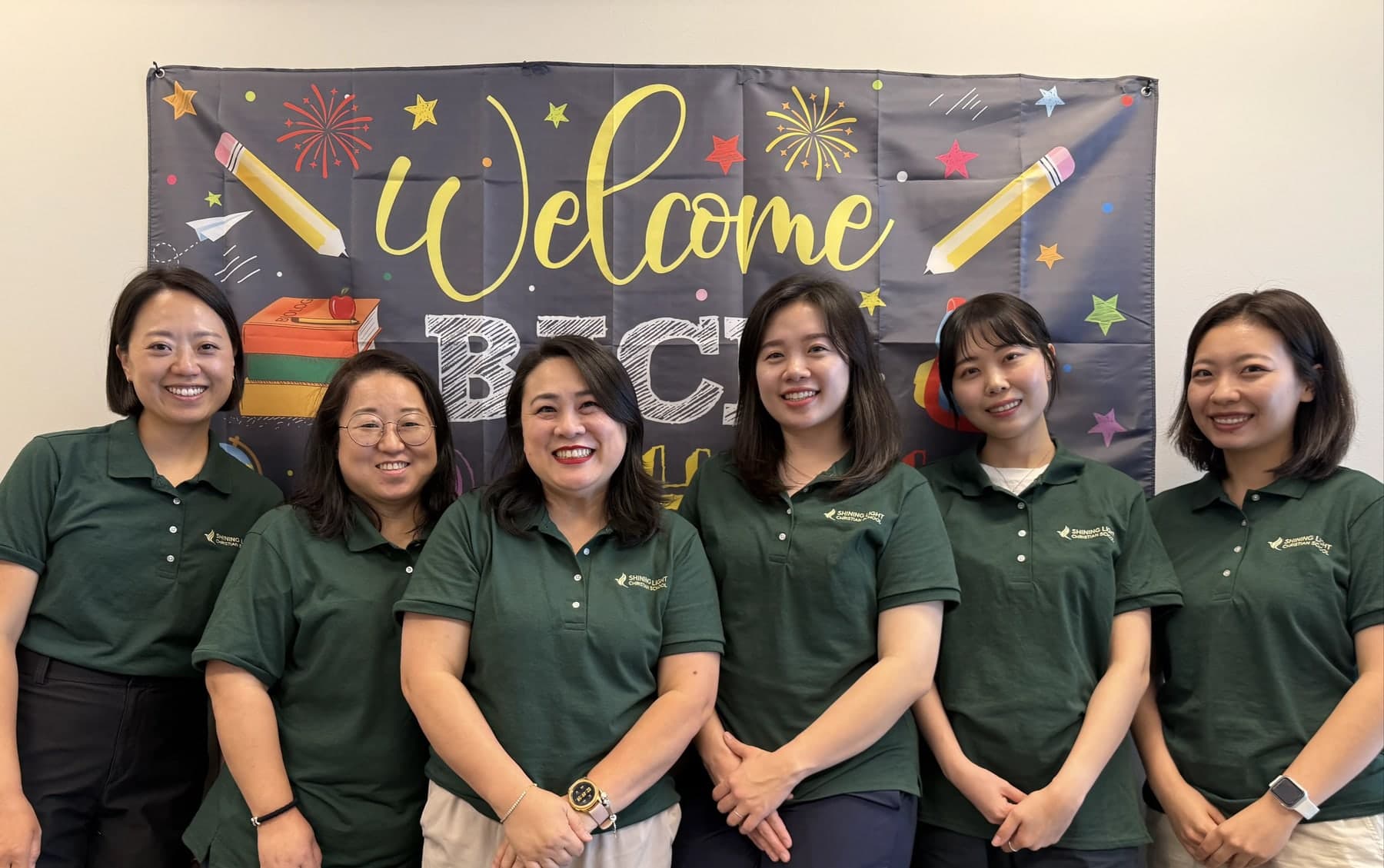 The Shining Light teaching team in school polos in front of a Welcome Back banner